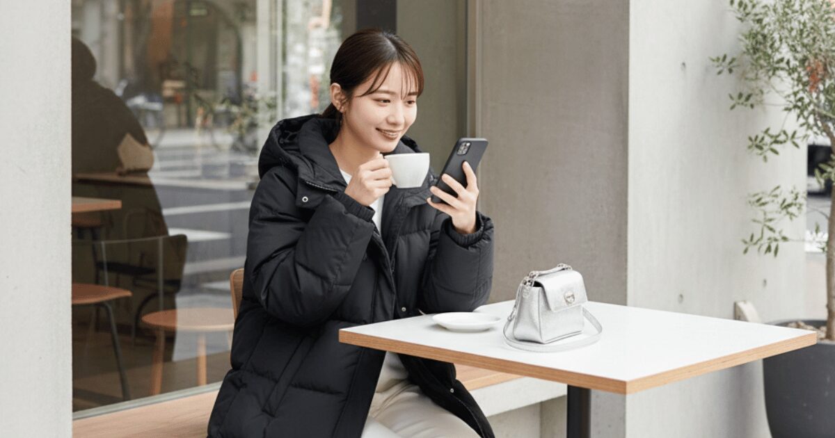 カフェのテラス席でコーヒーを飲みながらスマートフォンを操作する女性