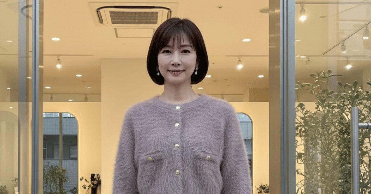 明るい店内の入口に立つ、ボブヘアで淡いカラーのニットを着た女性の全身写真
